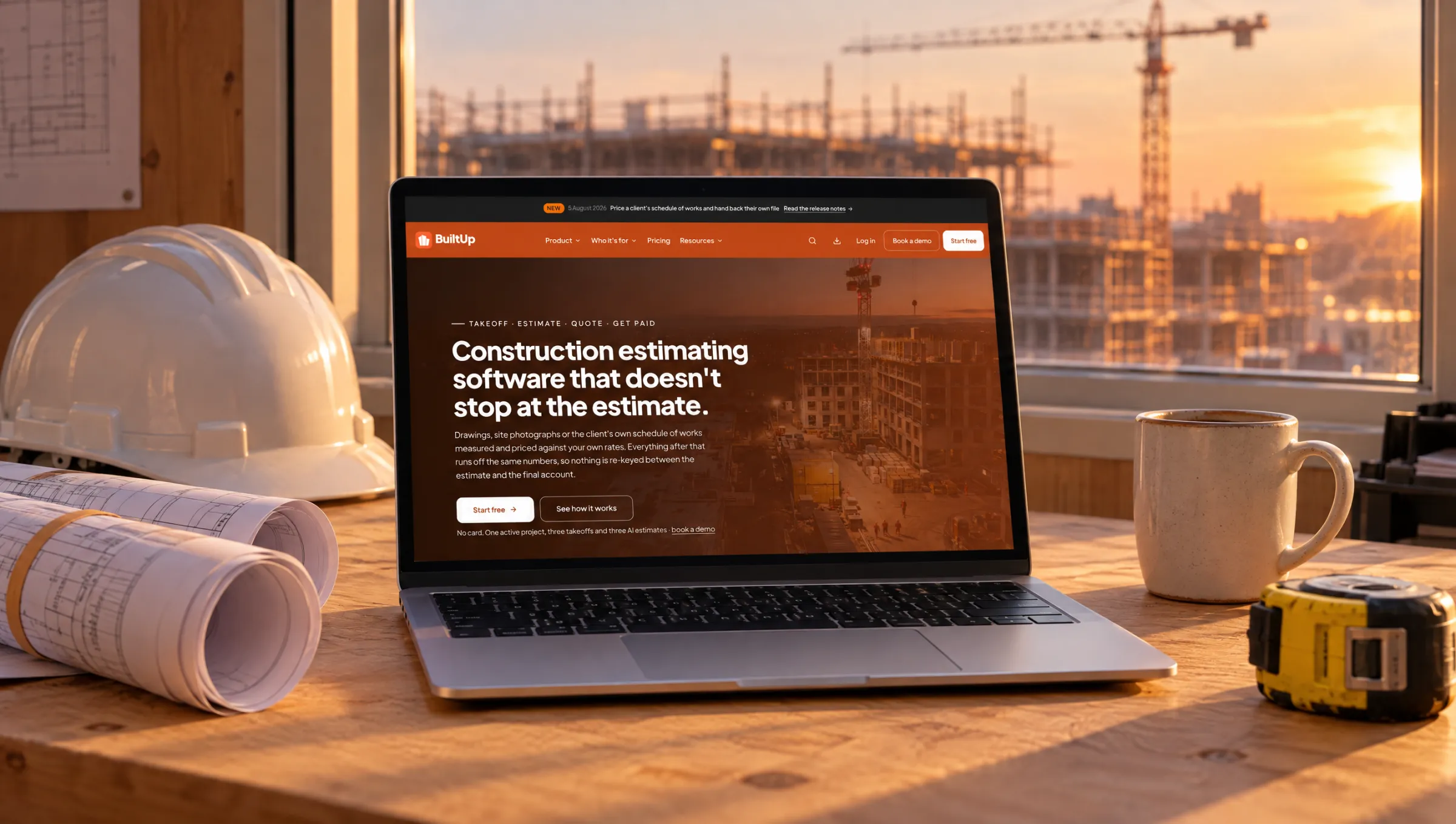 The builtup.io homepage open on a laptop in a site office, beside a hard hat, rolled drawings and a tape measure