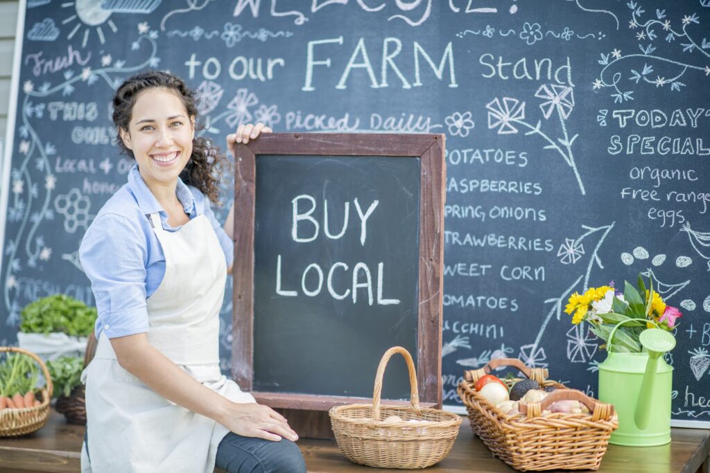 A girl sitting on a table holding a buy local sign