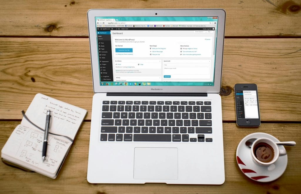 WordPress on a laptop screen on a coffee table with a notepad next to it with a cup of coffee